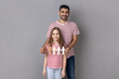 Portrait of father and daughter in striped T-shirts holding paper chain. Stop racism, social exclusion message, misunderstanding, denial of society. Indoor studio shot isolated on gray background.