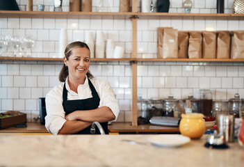 Canvas Print - Business owner, barista standing with arms crossed, looking confident and proud while working at a restaurant. Cafe worker, employee and entrepreneur smiling, giving service and leading a coffee shop