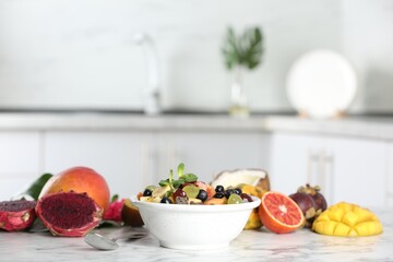 Delicious exotic fruit salad and ingredients on white marble table in kitchen