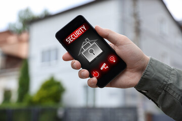 Man using home security application on smartphone in front of house outdoors, closeup
