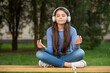Meditating teen girl listening to music in headphones meditating on bench outdoors, meditating