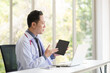 © Supagrit Ninkaesorn - Asian Doctor man sitting and using laptop in modern workplace office.