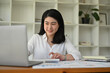 © bongkarn - Successful Asian businesswoman at her office desk managing her tasks on her laptop.