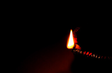 Wall Mural - Close up image of a lit clay diya or lamp on floor on Diwali - an Indian hindu festival of lights isolated on black background.