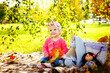 A little girl is sitting on the ground on a blanket. A kid on a picnic in a sunny autumn park.
