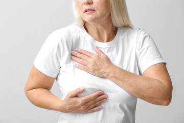 Wall Mural - Mature woman suffering from breast pain on light background, closeup