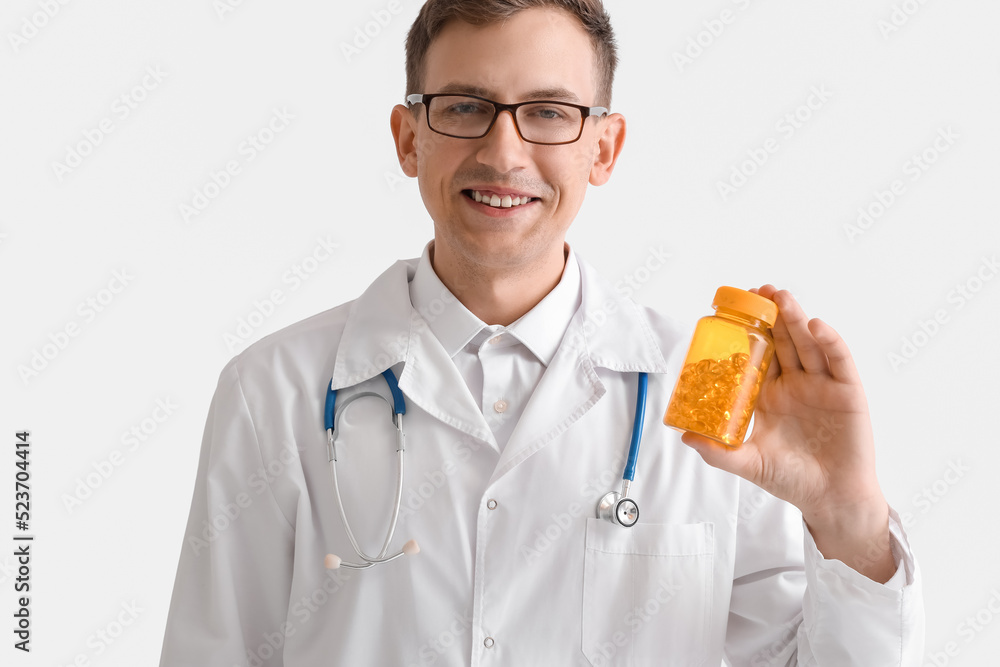 Young doctor with pill bottle on white background