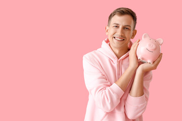 Canvas Print - Smiling young man with piggy bank on pink background