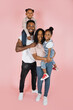 © sofiko14 - Spending time with family is fun. Full body length of excited african american man, woman and girls laughing and posing isolated on pink studio wall. Cheerful father carrying daughter on back, banner