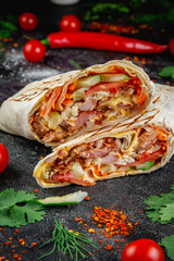 Wall Mural - Shawarma, burrito cut with vegetables and herbs on a dark stone table. The concept of fast food restaurants
