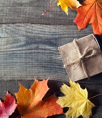 Wall Mural - cardboard box tied with string on a bow on a wooden background in autumn leaves, holiday gift on Thanksgiving Hellouin. view from the top. copy space