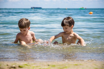 Wall Mural - Happy family playing in blue water of swimming pool on a tropical resort at the sea. Summer vacations concept. Two brother kids are best friends