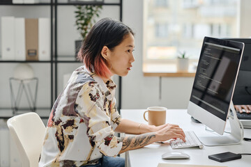 asian young girl sitting at her workplace in front of computer monitor and typing codes working at o
