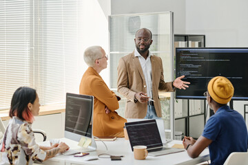 African businessman standing near the screen with presentation and presenting new software to programmers at meeting