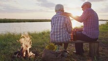 Old Affectionate Spouses Together Hug Sitting On Pond Shore Near Bonfire, Contemplating Nature Beauty At Sunset Outdoor. Real Love, Care And Support, Calm Family Relax, Happy Nostalgia At Evening Walk