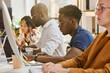 © AnnaStills - Group of programmers sitting at table in a row and writing codes on computers