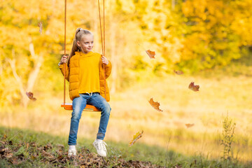 Happy little blonde caucasian girl smiling and riding a rope swing in autumn in the park.