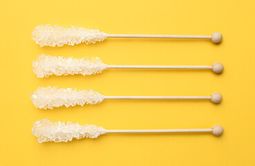 Poster - Wooden sticks with sugar crystals on yellow background, flat lay. Tasty rock candies