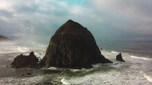Aerial Drone Flying Over Haystack Rock, Cannon Beach, Oregon, USA. Dramatic Cloudy Sunny Day. Ocean Waves Crashing. Rocky Cliff. Coastline. High Quality 4k Footage