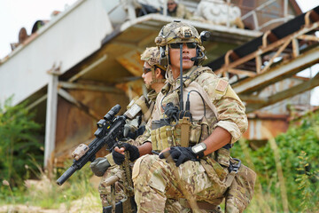 2 Army military soldier in the battle field sitting knee down on the ground hold the gun alert look around ready to fire weapon 
