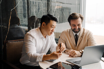 Adult multiracial businessmen using laptop while sitting by table