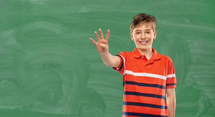 school, education and count concept - portrait of happy smiling boy in red polo t-shirt showing four fingers over green chalkboard background