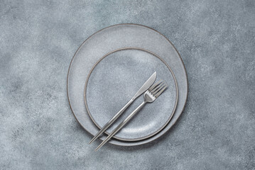 Gray plates with cutlery on a gray concrete background. Minimal table setting. Trendy ceramic dishes. Top view, flat lay.