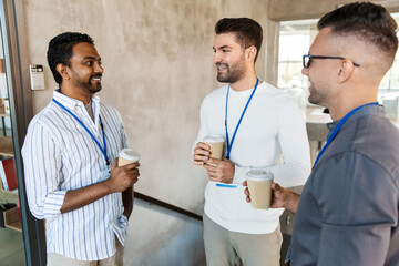 Wall Mural - business, people and corporate concept - happy smiling businessmen or male colleagues with name tags drinking takeaway coffee at office