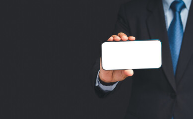 Wall Mural - businessman in a suit holding a blank screen smartphone while standing on a black background