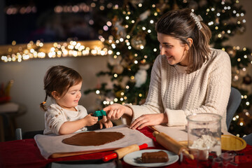 Poster - family, cooking and winter holidays concept - happy mother and baby daughter with mold making gingerbread cookies from dough at home on christmas