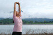 © Pornpimon - Asian woman warming up and stretching her arms in the riverside countryside in the morning before jogging. Sports and recreation healthy lifestyle concept.