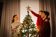 © Syda Productions - family, winter holidays and people concept - happy mother, father and little daughter decorating christmas tree at home