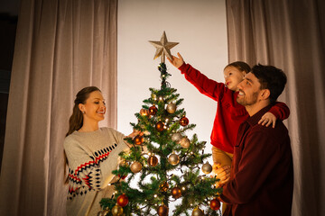 family, winter holidays and people concept - happy mother, father and little daughter decorating christmas tree at home