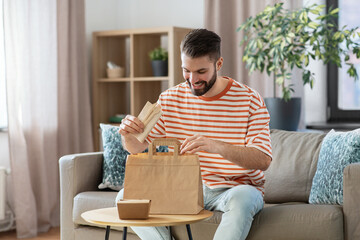 Poster - consumption, eating and people concept - smiling man unpacking takeaway food in paper bag at home