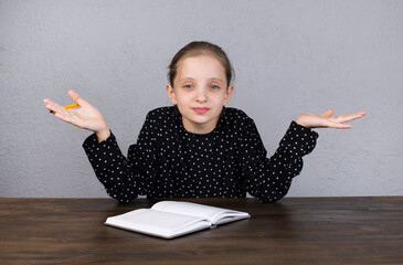 Wall Mural - Cheerful European girl. The girl does her homework while sitting at the table. Holds hands to the sides.