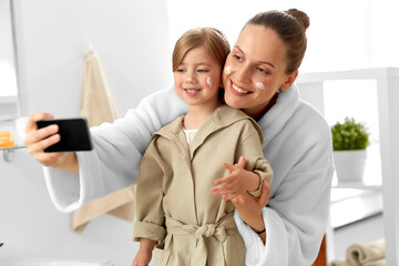 Sticker - beauty, family and people concept - happy smiling mother and daughter with moisturizer on their faces taking selfie with smartphone in bathroom