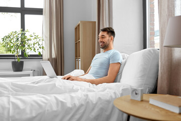 Sticker - people, technology and remote job concept - man with laptop computer lying in bed at home bedroom