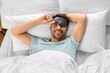 © Syda Productions - people, bedtime and rest concept - happy smiling man in sleeping eye mask lying in bed, top view