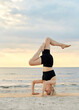 fitness, sport, and healthy lifestyle concept - woman doing yoga headstand on beach over sunset
