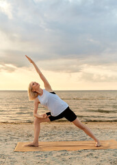 Canvas Print - fitness, sport, and healthy lifestyle concept - woman doing yoga triangle pose on beach over sunset