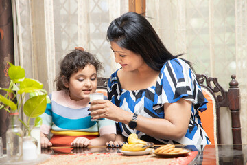 happy Indian asian family mother and cute little daughter drink milk having breakfast in kitchen, healthy diet, protein and calcium