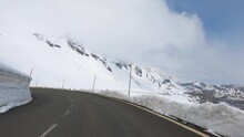 Dizzying Time-lapse of driving over a wet asphalt road in the high Alps with remnants of snow on the embankments next to the road, POV.