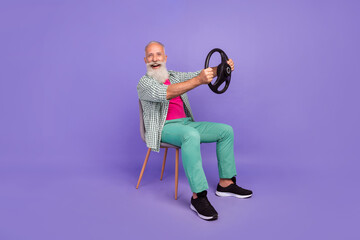 Full size portrait of excited cheerful aged person sit chair hold wheel isolated on purple color background