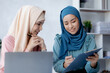 © kamiphotos - Two hijab-clad Asian women are brainstorming together in a conference room for a startup, run by a young, talented woman. The management concept runs the company of female leaders to grow the company.
