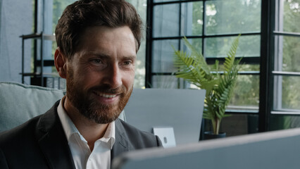 Close-up male worker leader Caucasian businessman bearded mature adult 40s manager looking at window smiling working with computer think about idea chatting online browsing programming job with smile
