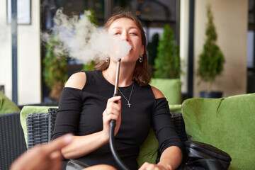 Image of a beautiful woman smoking a hookah in a lounge bar. Vacation concept.