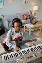 Wall Mural - Vertical portrait of black young woman playing music at home and wearing headphones