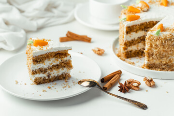Wall Mural - Delicious carrot cake decorated with mastic sweet carrots next to white cup of tea. Slice of homemade carrot cake with yellow crumbs in the white plate on the white background