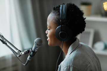 Minimal side view of young female musician singing to microphone at home and wearing headphones, copy space