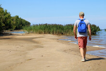 A Man With A Backpack Walks Along A Wild Beach.